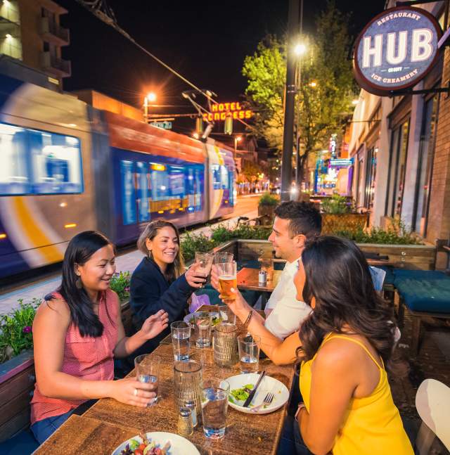 Three women and one man dining outdoors at Hub Restaurant downtown at night