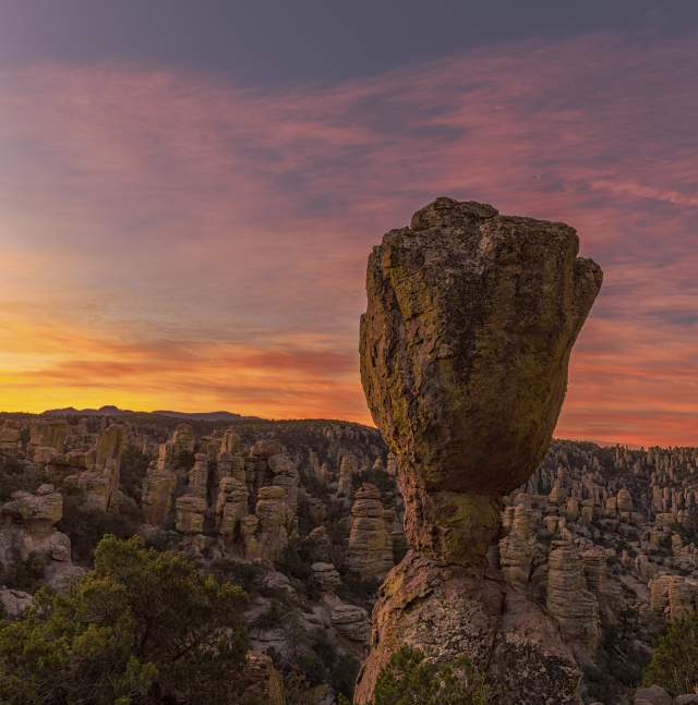 Large oblong rock formation standing tall above a field of similar odd-shaped rock formations at sunset