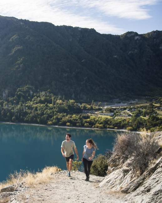 Two people walking to the top of Bob's Cove with views of the turquoise bay behind them