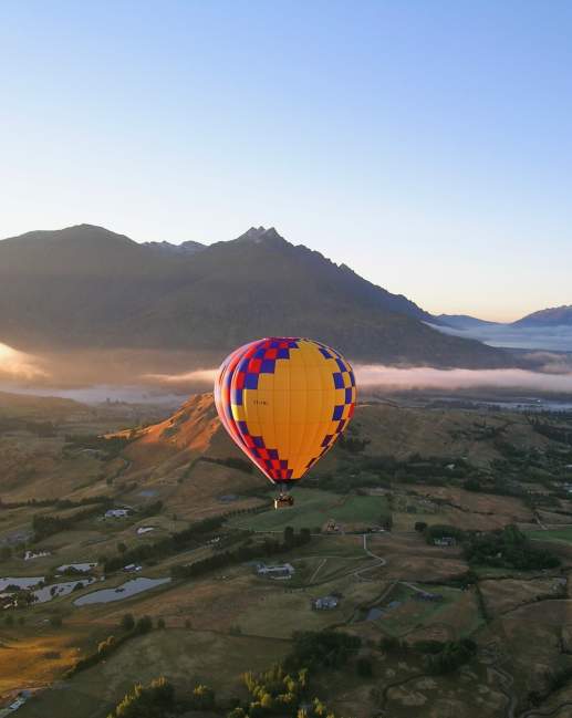 Shot of a hot air balloon at sunrise overlooking a green valley and mountain