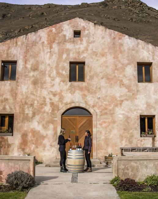 A person having a wine tasting outside Chard Farm Cellar door, a dusty pink Mediterranean style building