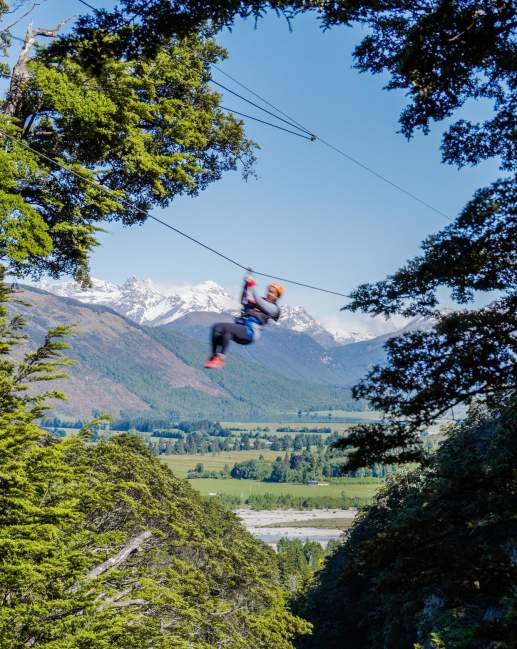 Person ziplining with snow-covered mountain in the back