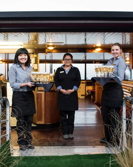 Waitresses waiting to greet guests onto a boat with trays of champagne
