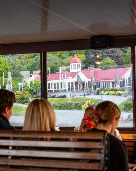 A group of people sitting on the TSS Earnslaw with a view of Walter Peak through the windows