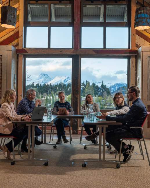 A small group of people sitting around a conference table with view of mountains and trees from the window