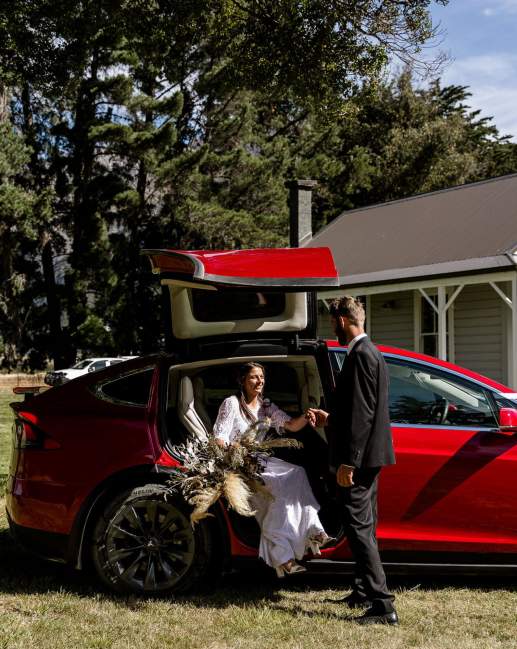 A couple at their wedding step out of a red Tesla vehicle