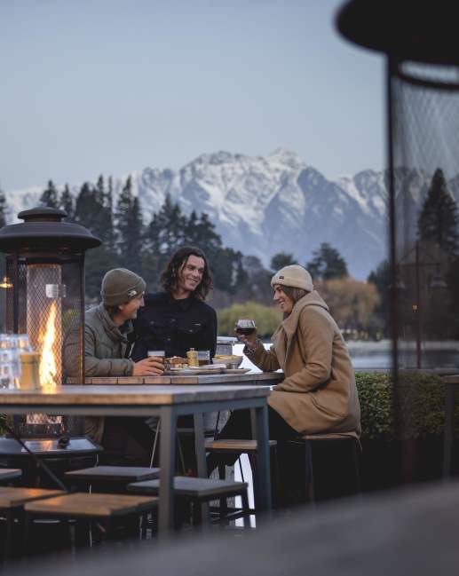 Friends dining outdoors in winter with Remarkables mountain in the background