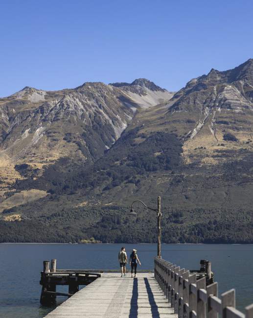 Two people standing on Glenorchy Wharf with mountains in the background