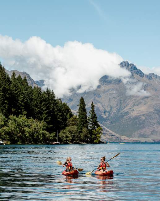 Two people kayaking in Queenstown Bay with mountains in the background