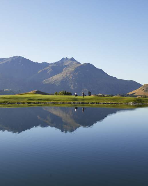 Wide shot of a golf course with lake reflecting mountains