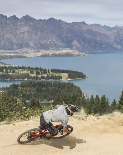 Person biking Queenstown Bike Park with view overlooking lake Whakatipu and the Remarkables mountain ranges