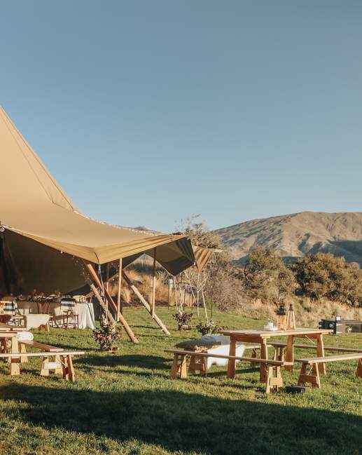 A tipi set up on a farm with mountains surrounding