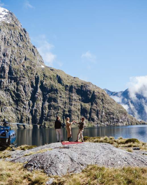 People having a picnic next to a high alpine lake with a helicopter next to them