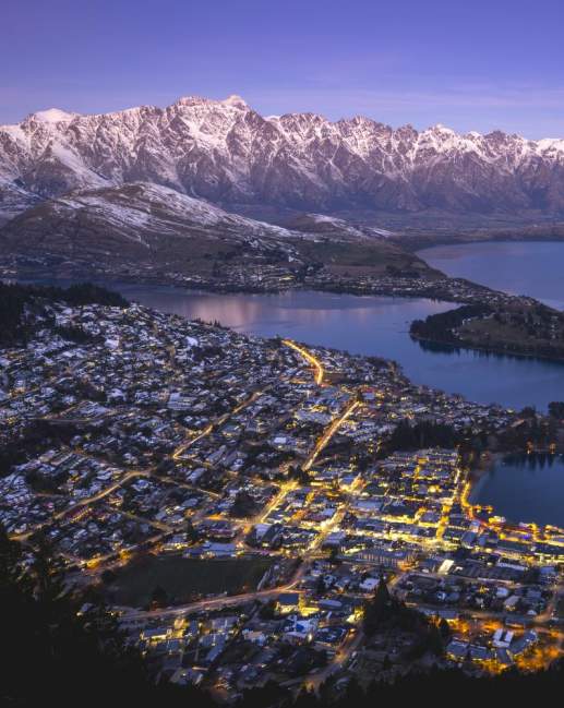 Aerial shot of Queenstown on a winters evening with town street lights glowing and snow capped mountains in the background