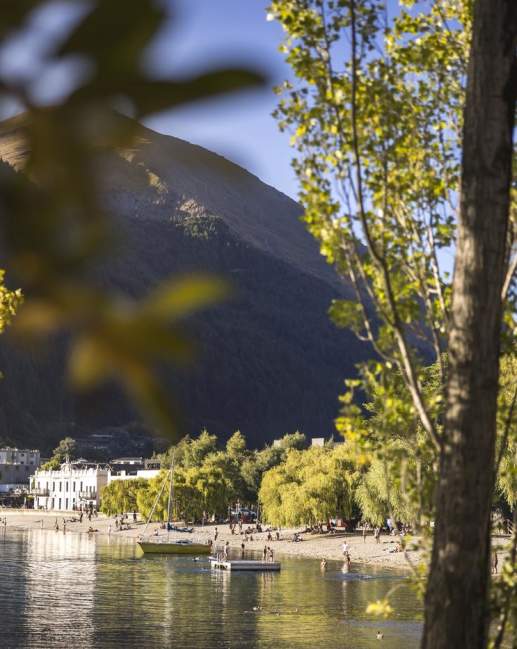 Looking through green trees to big lake, boats, people and buildings
