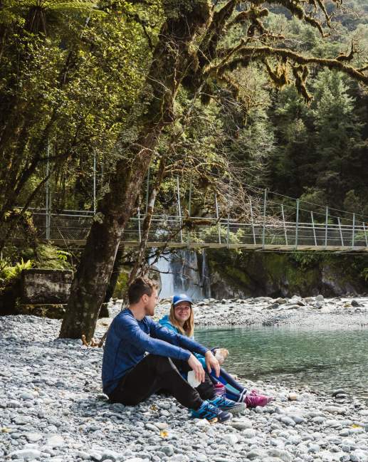 Two people sitting next of a river surrounded by bush