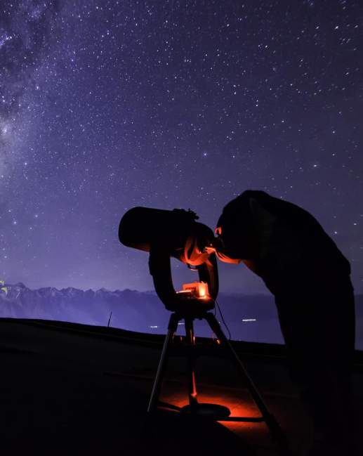 Person with telescope stargazing underneath the milky way near The Remarkables mountain range