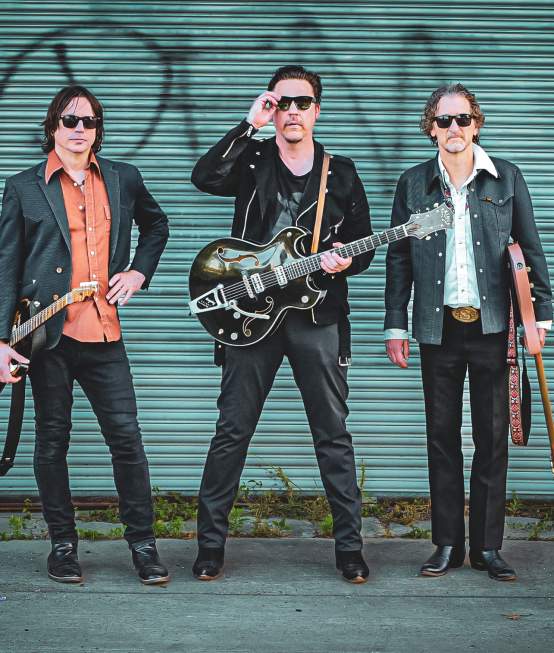 Three-piece band with guitars pose in front of a closed green tagged garage door