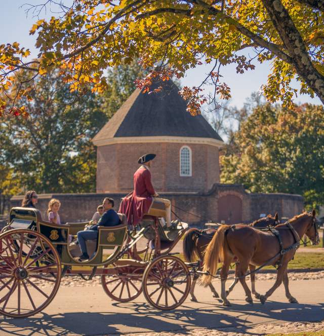 A horse-drawn carriage passes under colorful autumn leaves, with a historic round building in the background, evoking a charming, nostalgic atmosphere.