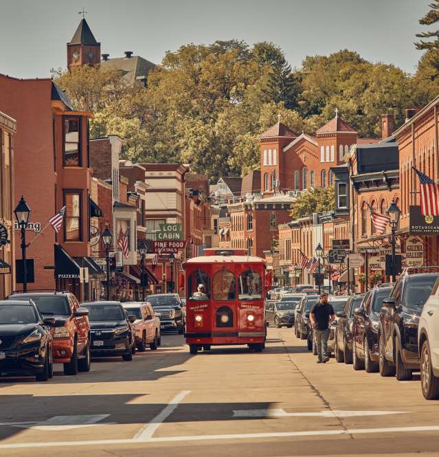 Image of downtown Galena, on its Main Street. Photo includes a red trolley bus driving on the street with red brick buildings on both sides.