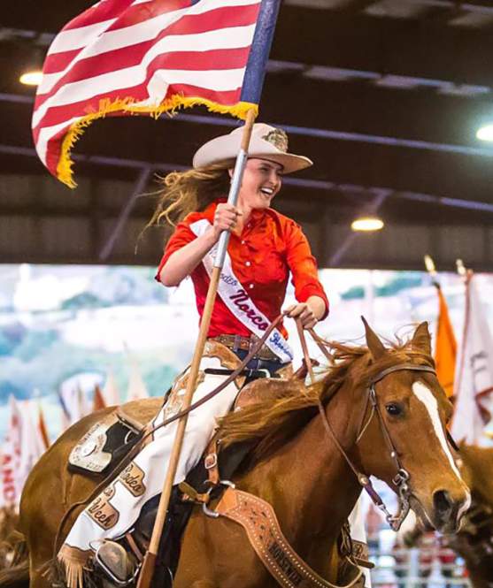 Woman holding an American flag while riding a horse at the rodeo in Norco, CA