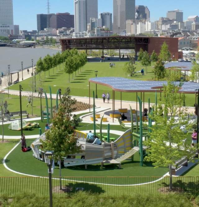 An aeriel view of the Goldring Woldenberg Riverfront Park along the Mississippi River in New Orleans' French Quarter. This shot shows the playground area with the covered performance space and city skyline in the background.