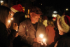 A man with a candle in hand smiles to those around with santa hats on and candles also at night during the Old Golden Holidays Candlelight Walk 2024.