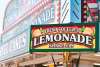 A man stands under a food kiosk that reads lemonade