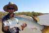 A man in a tinny holding a freshly caught barra, in a creek near Port Hedland