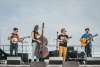 A band of four people—one with a banjo, cello, ukelele, and guitar—stands on stage on the beach.