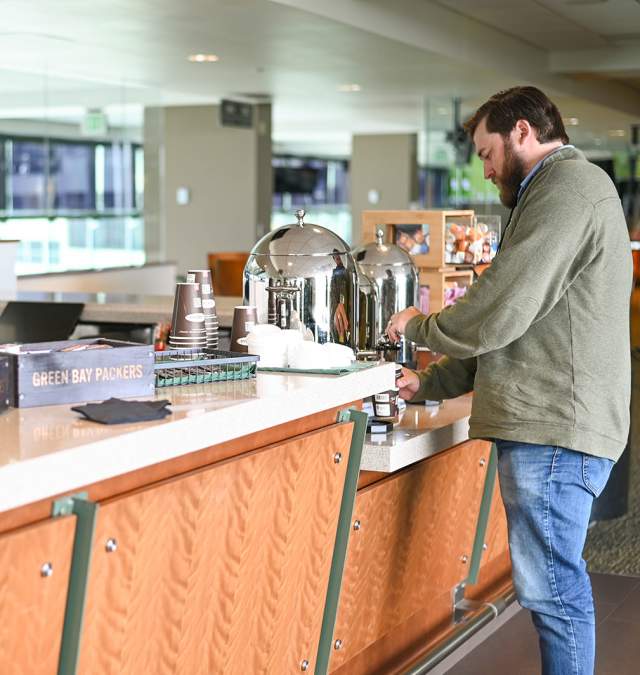 A man attending a conference at lambeau field pours coffe from the refreshment area.