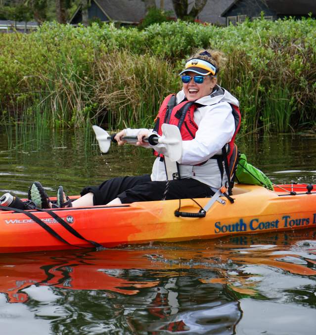 a person sits smiling in a kayak on the water