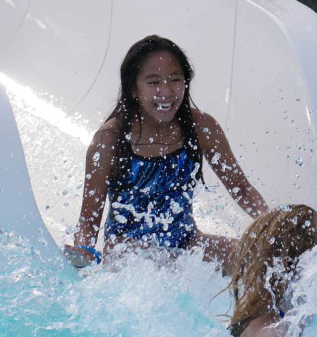 A smiling girl with dark hair splashed into the pool at the end of a waterslide.