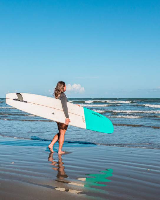 Girl holding a white and blue surf board walking into the water.