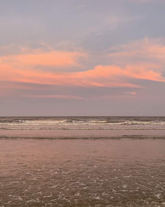 A pink and blue sunset sky reflects off the water on the beach
