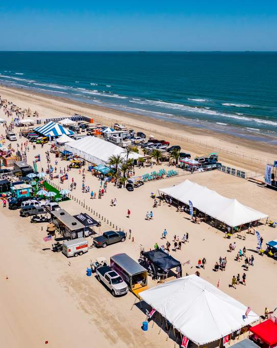 Aerial shot of a long stretch of beach covered in tents and people during a festival.