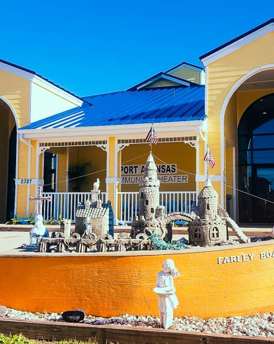 Yellow Farley boat with a small sandcastle inside sits in front of a large yellow building with a blue metal roof