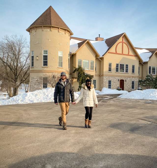 Couple holding hands, standing outside of a building surrounded by snow.