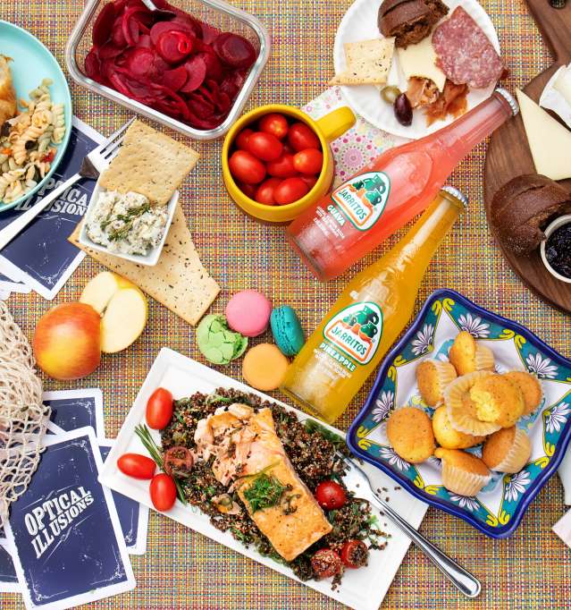 bottled sodas, charcuterie board with meats and cheeses, and various other foods on a table with cards.