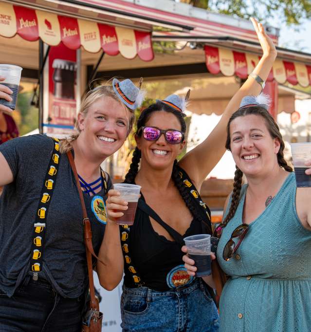 Three people holding beverages at a summertime event, outside.