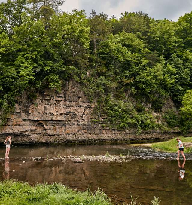 Two people fishing at a state park with a natural rock bluff behind them.