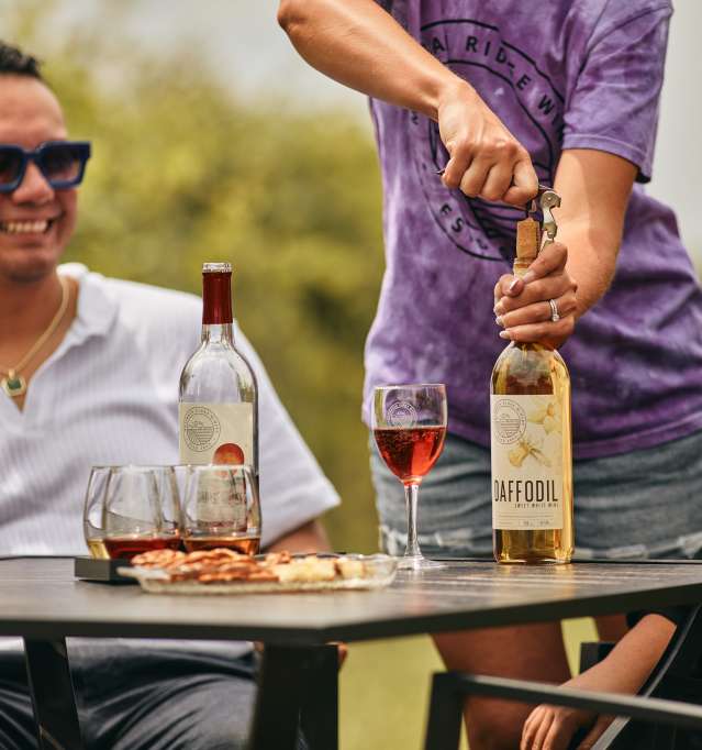 Two people sitting outside at a table, enjoying wine that is being poured for them.