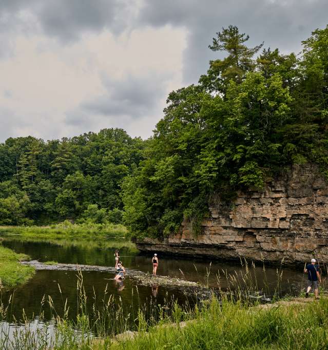 Three people fishing in a stream next to a bluff in a state park.