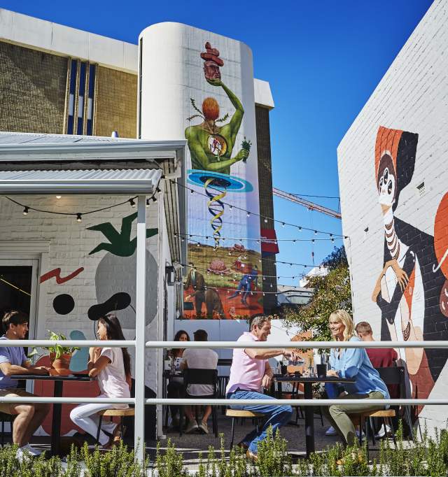 Groups of people eating, surrounded by street art on buildings