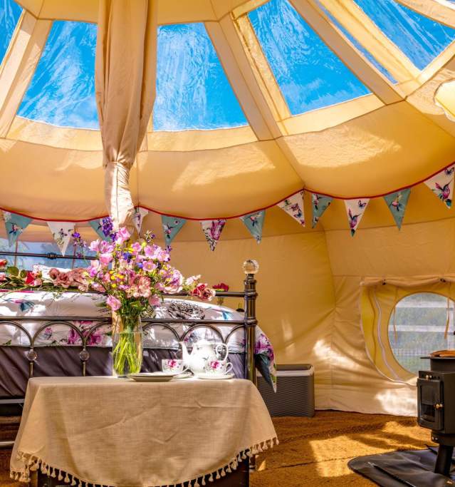 A glamping pod with woodburner and bed surrounded by flowers and bunting