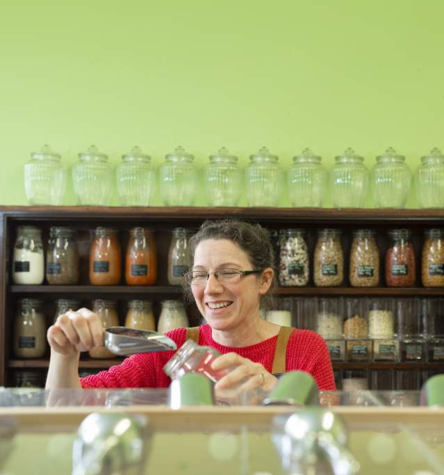 a woman pouring grain into a jar in a produce shop