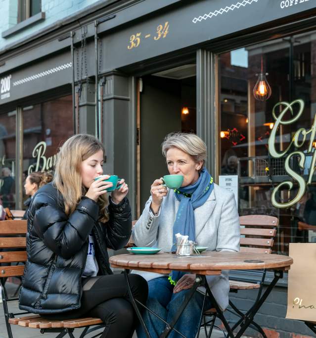 A mother and daughter enjoying coffee outside a cafe.