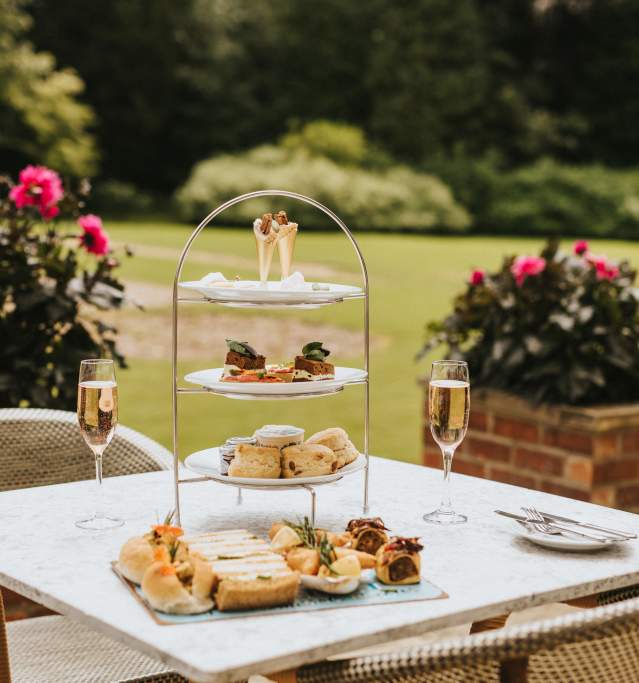 An afternoon tea display with Champaign on a outdoor seating table in gardens with flowers in background