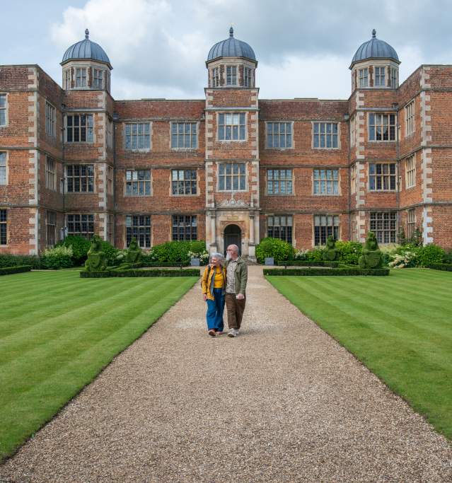 A couple walking in front of Doddington Hall, a heritage house with gardens.