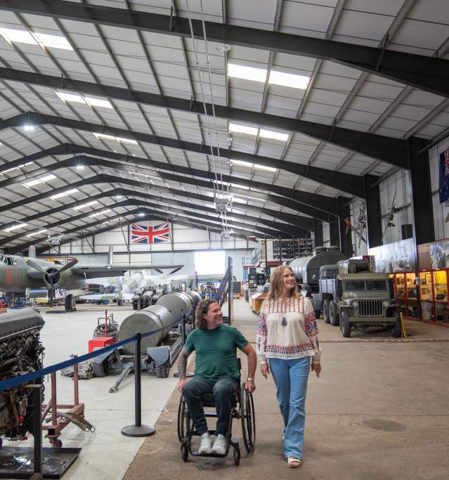 two people in a hanger with aviation props and planes in background